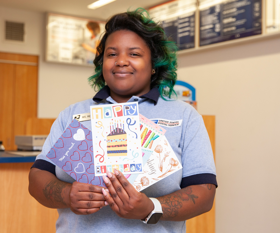 Smiling postal retail associate holds greeting cards