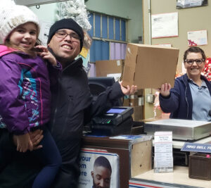 Smiling father with young daughter hand package to postal worker at retail counter