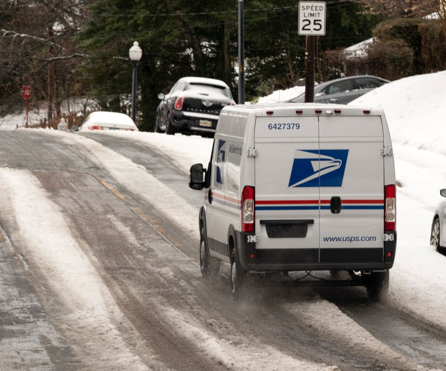Postal vehicle drives along a snow covered street.