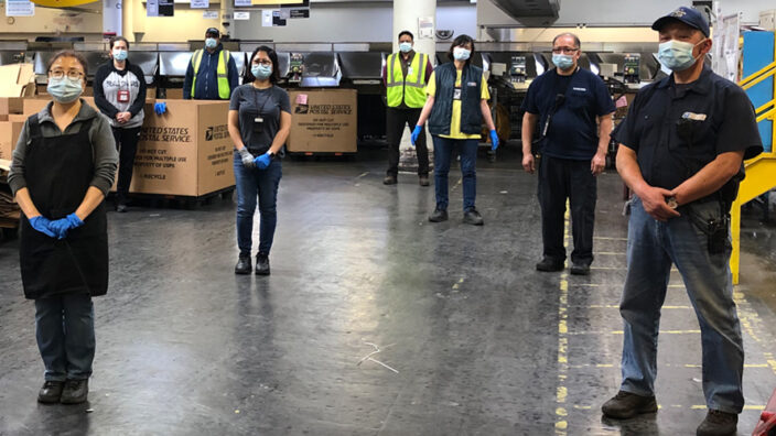 Postal employees standing in a USPS plant.