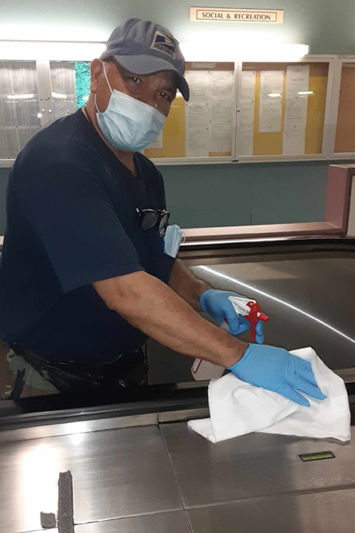 Face-masking wearing worker wipes down escalator handle