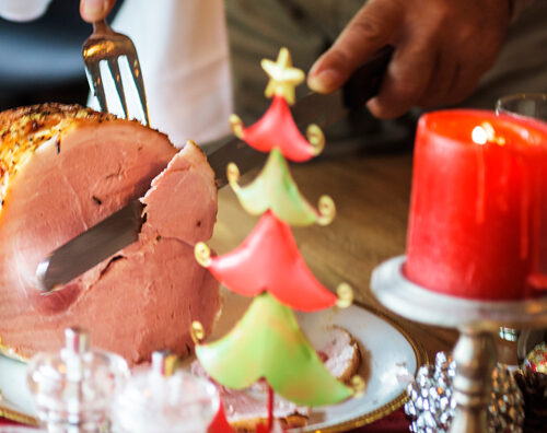 Man's hands slice ham on table with festive decor
