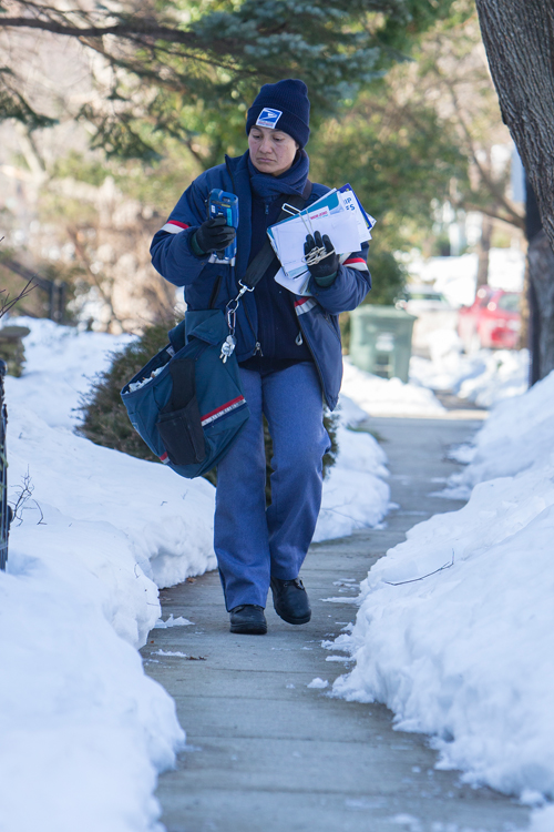 Postal worker walks along sidewalk after snowfall