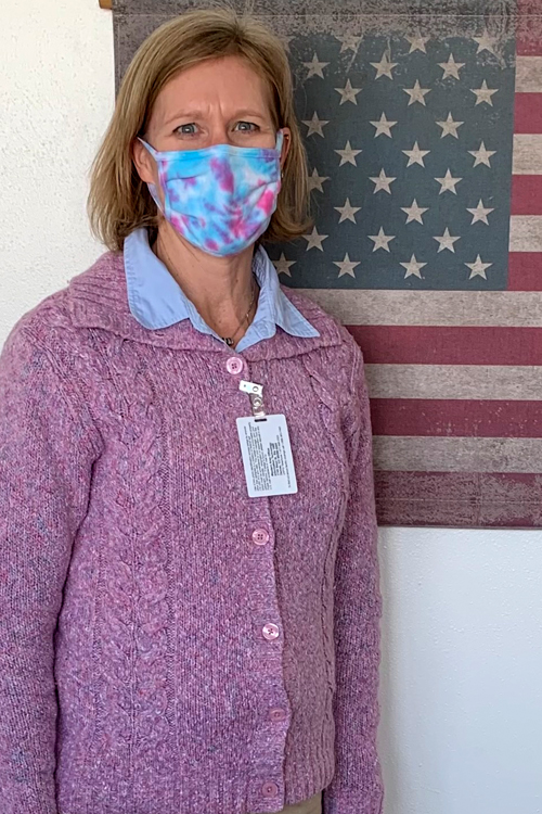 Masked woman stands next to flag