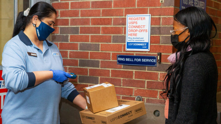 Postal worker scans package on loading dock as customer watches