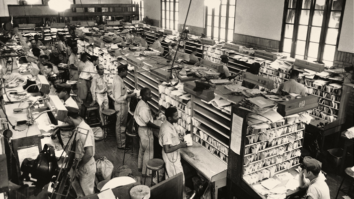 A black-and-white image of Black men sorting mail in a workroom