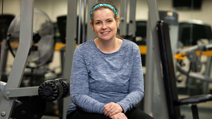 A smiling woman sits in a fitness room