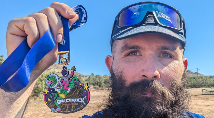Man wearing running gear holds medal in park setting
