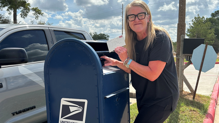 A woman places a letter in a blue U.S. Mail box