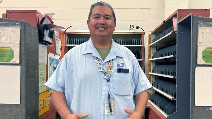 Smiling postal worker gives two thumbs up while standing in work room
