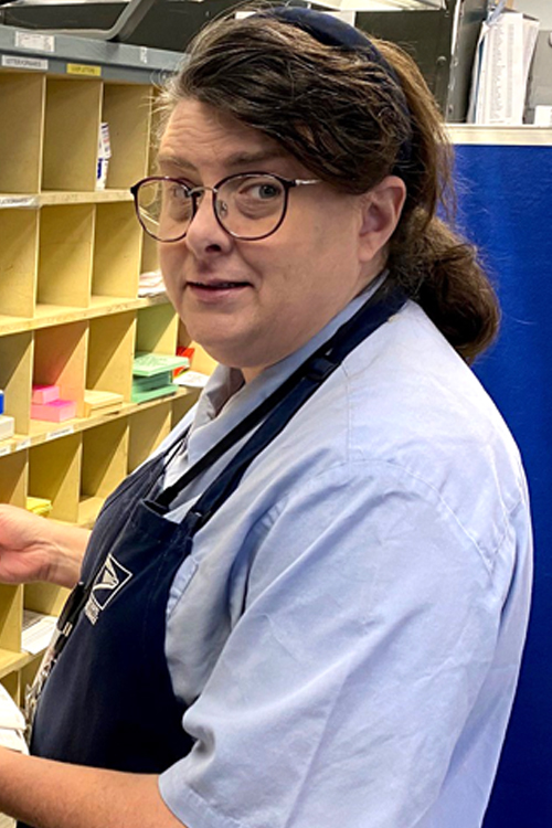 A woman in a postal uniform sorts mail at a cubby