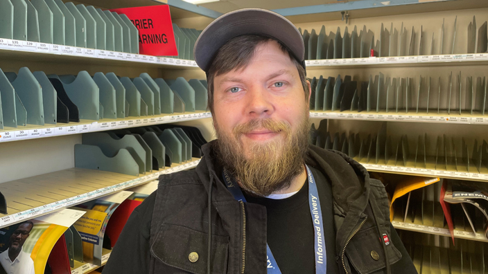 A smiling man stands in a Post Office workroom