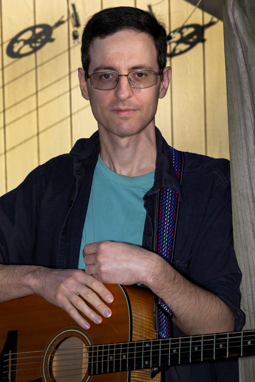 A smiling man holds a guitar