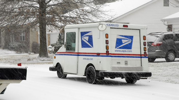 A postal delivery vehicle moves along a snow-covered street