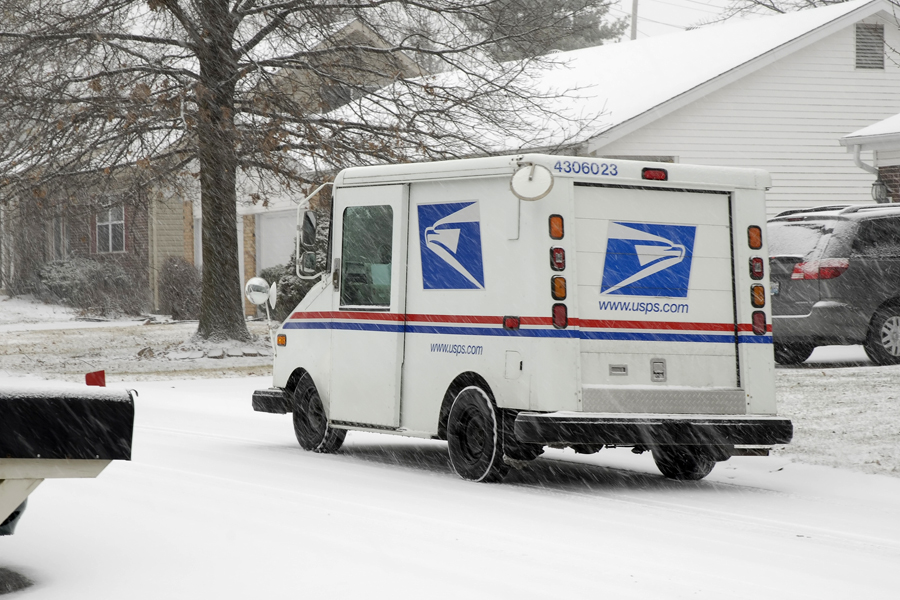 A postal delivery vehicle moves along a snow-covered street