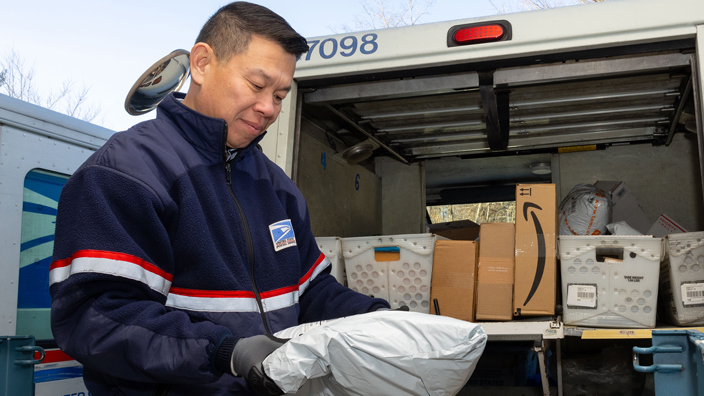 Man wearing postal uniform unloads packages from the back of a delivery vehicle
