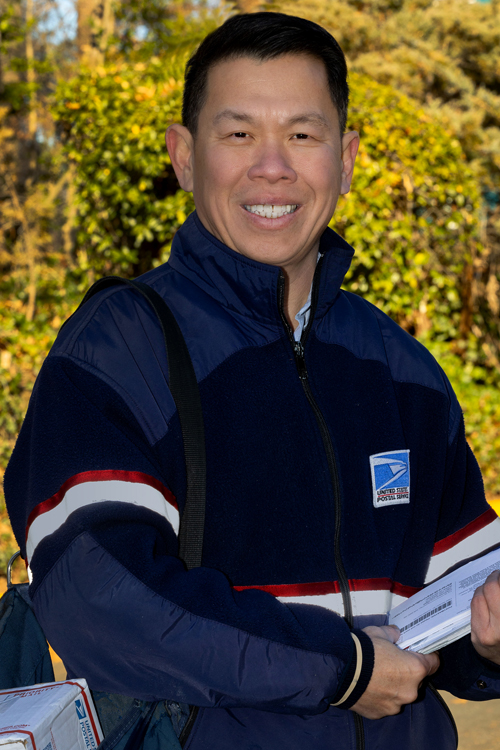 Man smiles while wearing postal uniform and holding a stack of mail