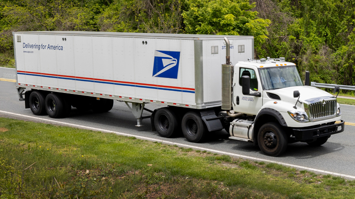 A USPS tractor-trailer drives along a highway