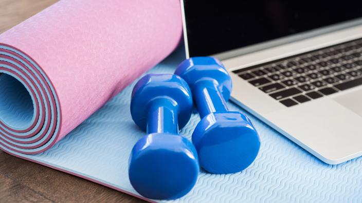 A laptop and dumbbells sitting on a workout mat