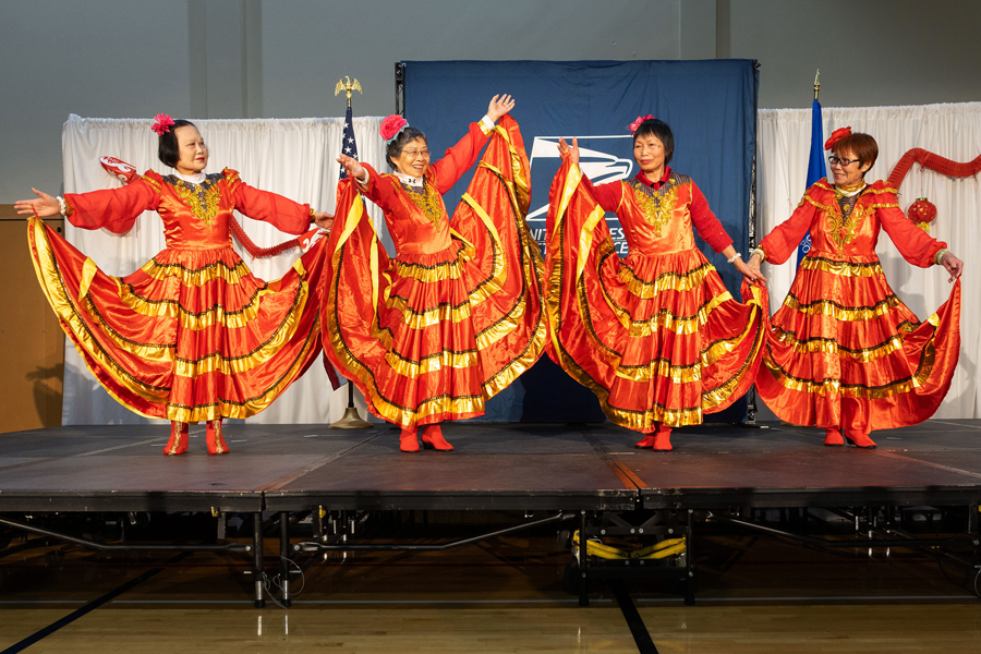 Four women wearing festive costumes perform a dance on a stage.