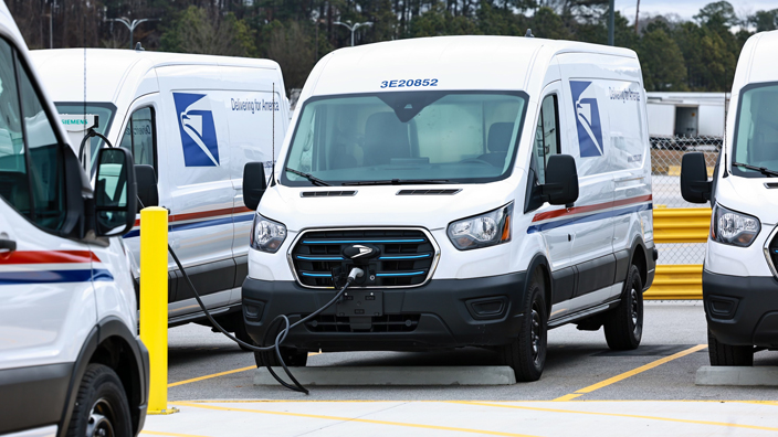 A white USPS delivery van at a charging station
