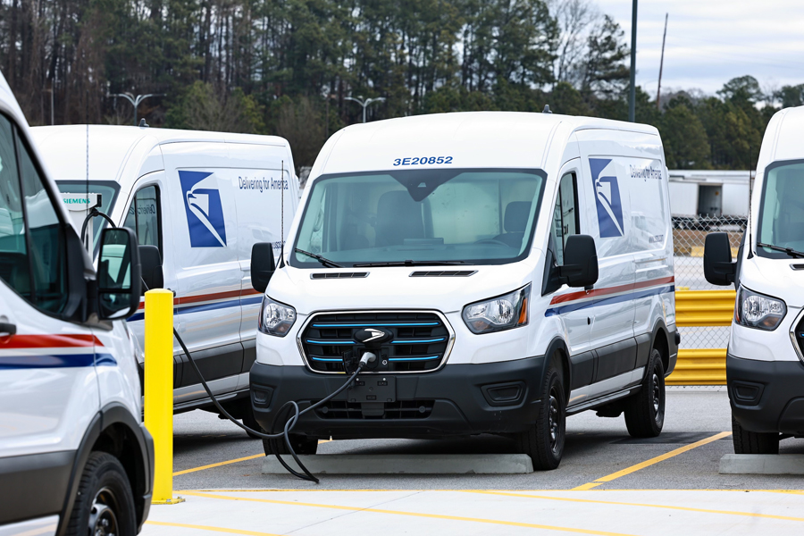 A white USPS delivery van at a charging station