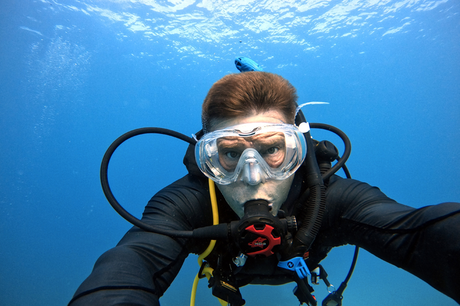 A man wearing scuba diving equipment floats under water