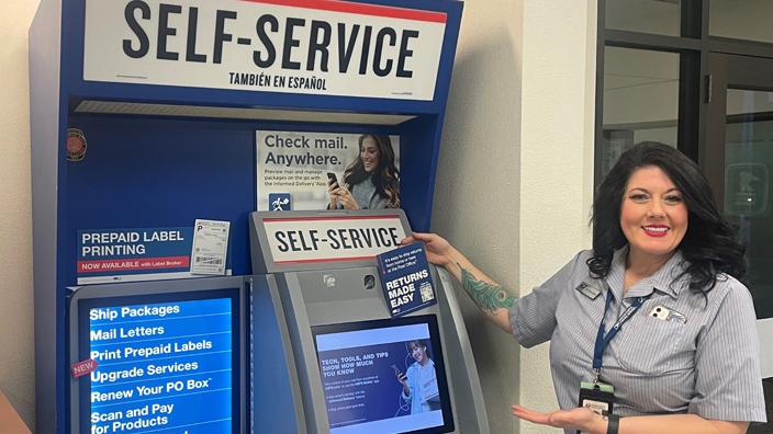 Smiling woman in postal uniform stands near self-service kiosk in Post Office lobby