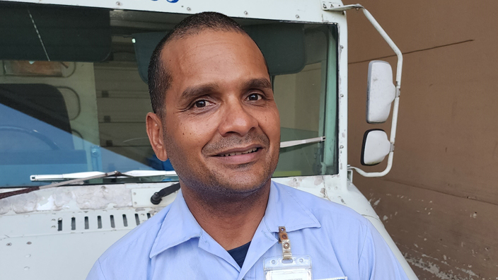 A smiling man in a postal uniform stands near a USPS delivery truck