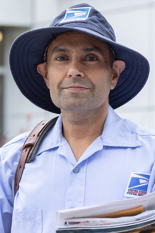Smiling man in postal uniform stands outside Post Office