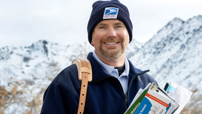 Smiling letter carrier delivering mail in snow