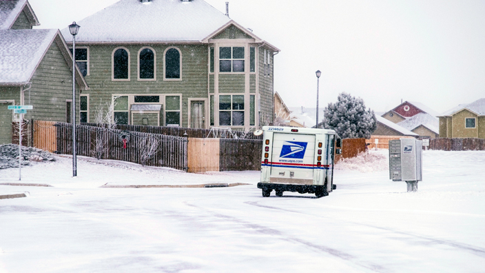 Postal delivery truck stops at a mailbox on a snowy residential street