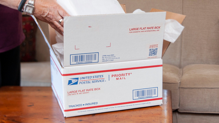 A person puts an item into a USPS Priority Mail box.