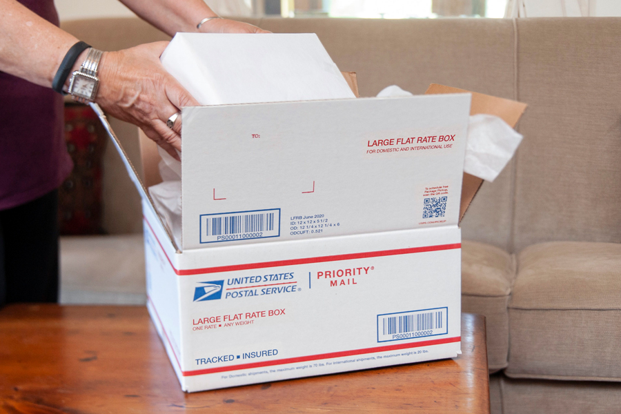 Woman's hands open Priority Mail box on coffee table in living room