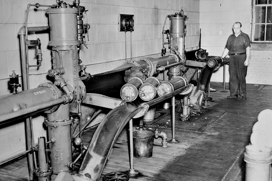 Black and white image of man standing near a network of tubes