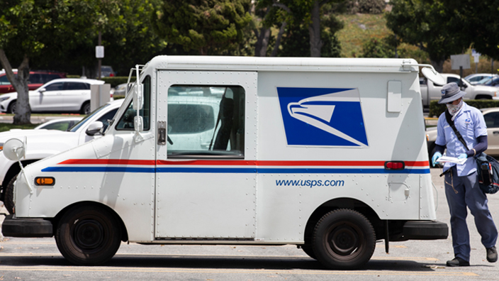 A male letter carrier delivering mail from an LLV