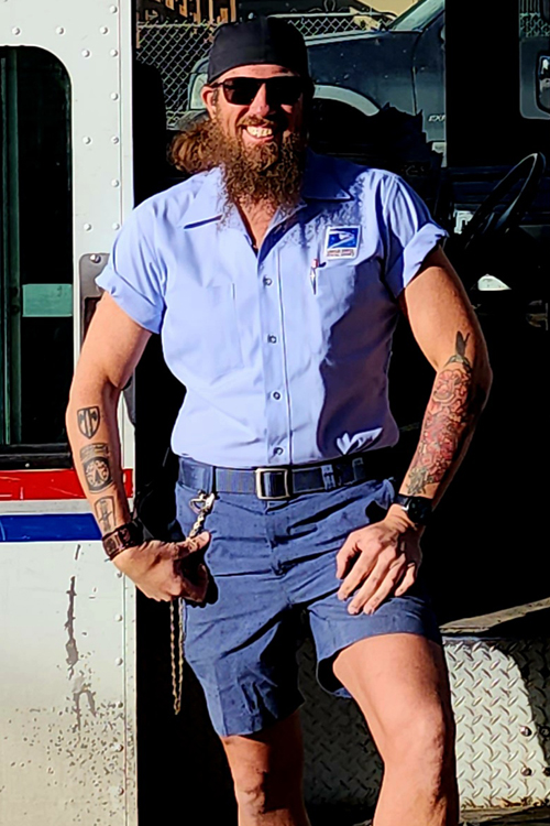 A male letter carrier smiling and standing outside a postal vehicle