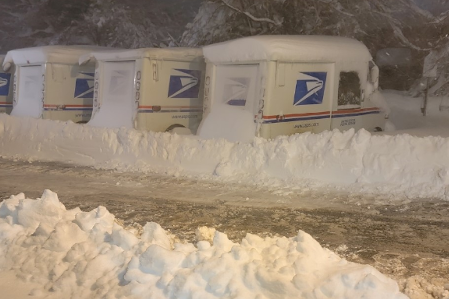 Postal delivery vehicles sit under heavy snow