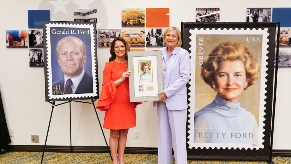 Two smiling women hold framed stamp artwork