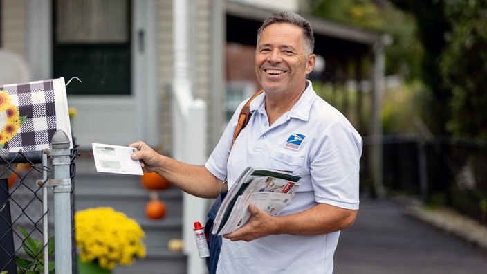 Smiling male letter carrier making a delivery to a mailbox