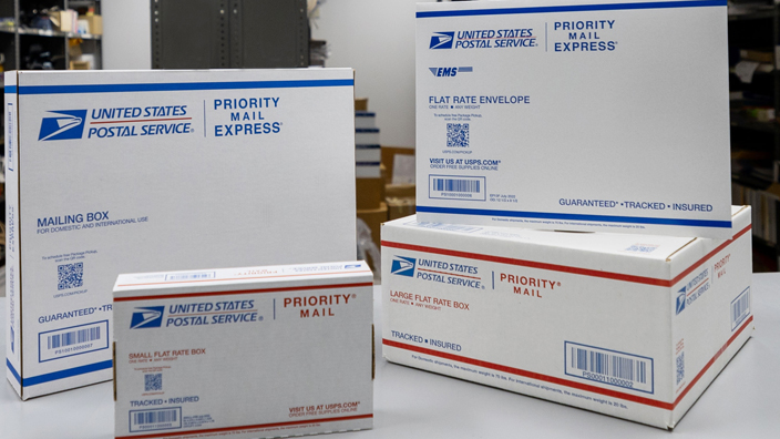 Priority Mail and Priority Mail boxes and envelopes are displayed on a table.