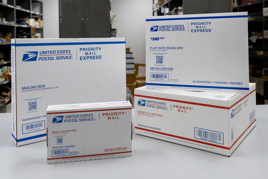 Priority Mail and Priority Mail Express boxes and envelopes are displayed on a table.