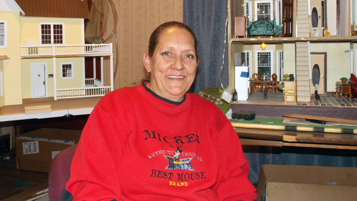 A woman in a red sweater sits next to a dollhouse