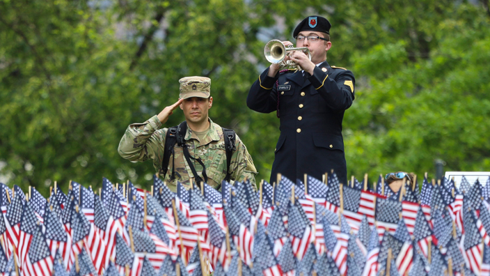 A soldier plays a trumpet while another soldier salutes.