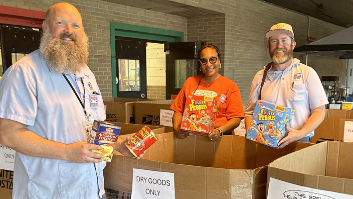 Two men and a woman fill boxes with canned and boxed food items.