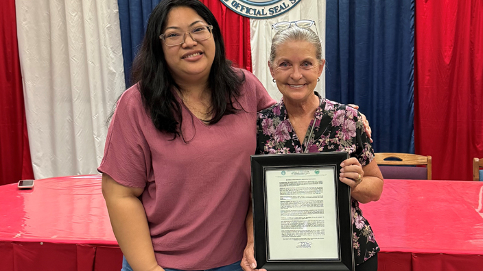 Rota Mayor Aubry Hocog, left, presents Tina Ramirez with a resolution honoring her service with USPS.