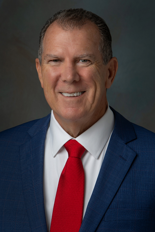A headshot of Bill Fraine wearing a blue jacket and red tie