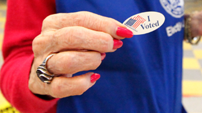 A worker at the polls displays an "I Voted" sticker