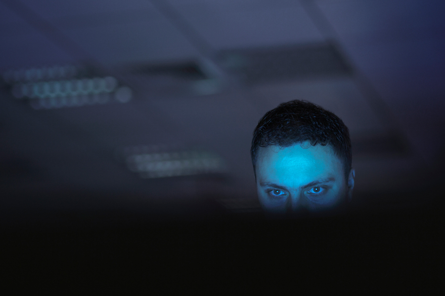 A man in the dark looking suspiscious in the glow of a computer screen