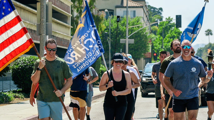 A group of participants run in formation carrying the torch and flags during an event for the Special Olympics